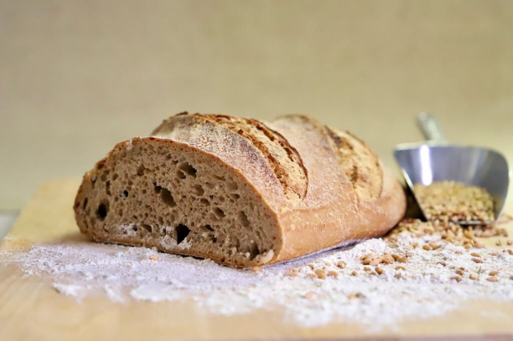 Artisan bread loaf on wooden board with scattered flour and grains.